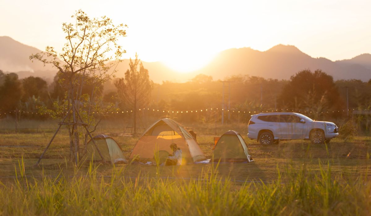 A sunrise in neature while tents are set up for camping with an SUV car next to the tents.