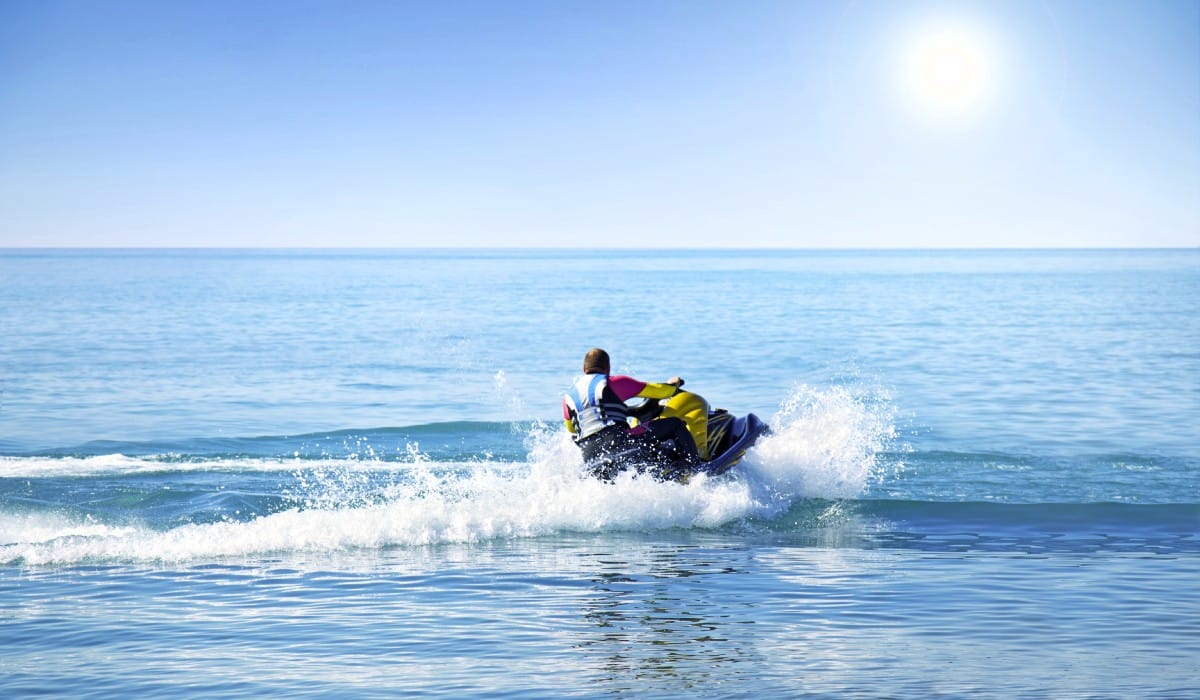 A rookie jet skier out on the water alone. They turn their ski, creating a wake in the water, while wearing a safety vest.