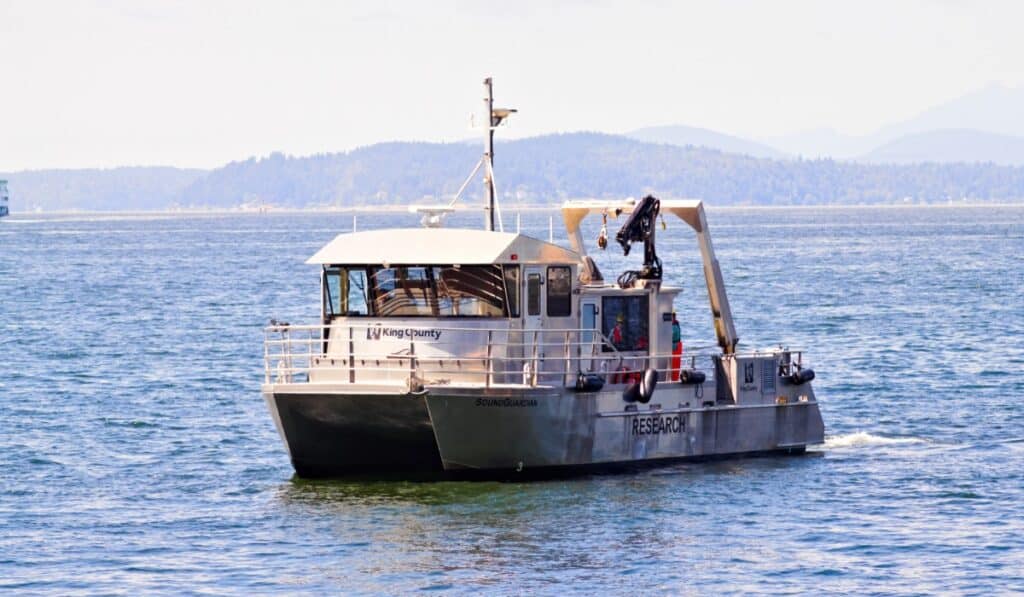 A vessel marked “King County” cruising on calm blue water, with distant forested hills in the background.