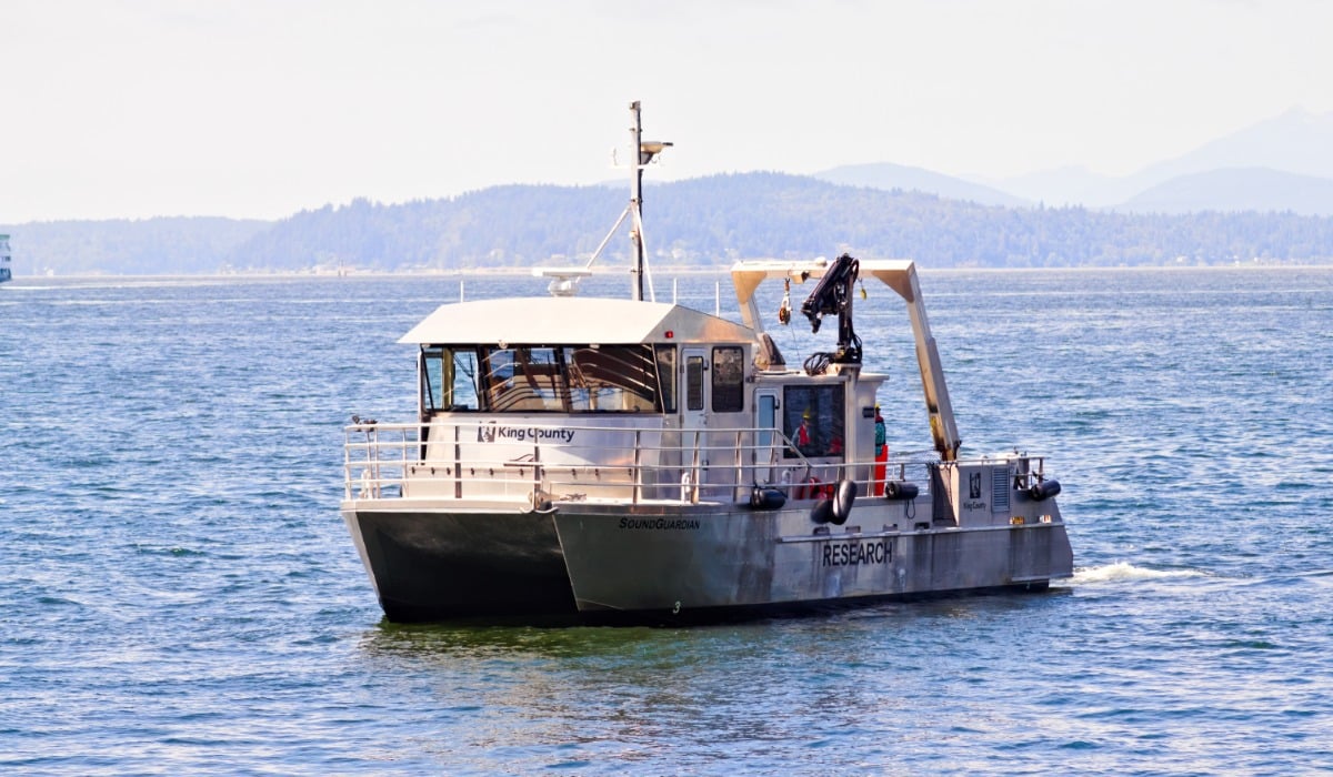 A vessel marked “King County” cruising on calm blue water, with distant forested hills in the background.