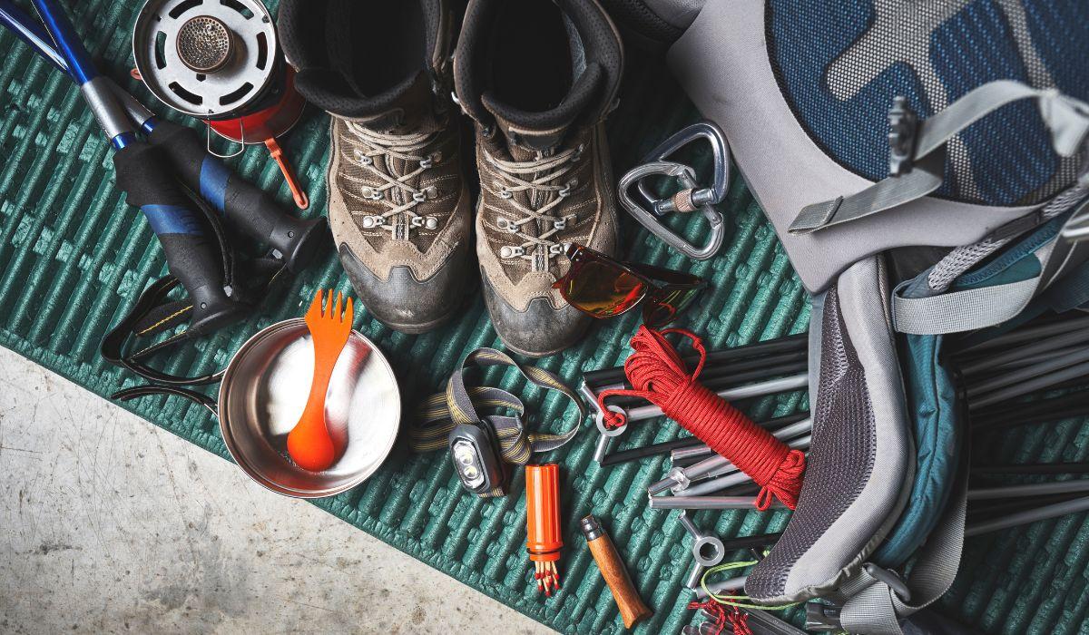 A green surface contains boots, a backpack, trekking poles, and camp tools that were cleaned after an outdoor trip.